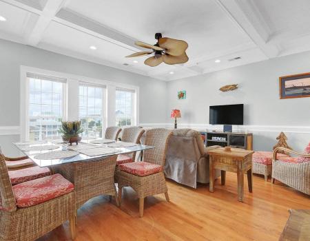 The open-concept living- and dining-room area at Oak Knot in Carolina Beach features three large windows, seating arrangements for six, and hardwood floors.