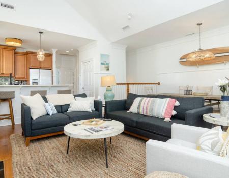 The open living room at Moore Shore Time in Wrightsville Beach, N.C. includes seating for six with a black loveseat, a black sofa, and a white armchair.